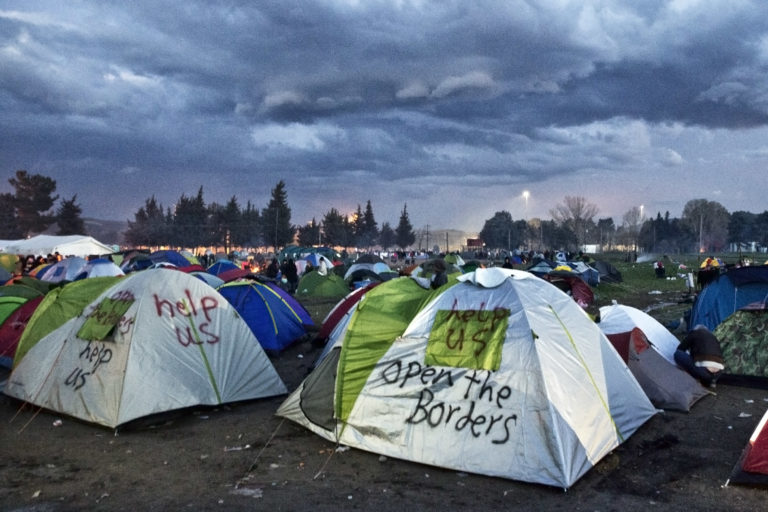 Zelte auf einer großen Wiese, beschriftet mit "help us" und "open the borders"